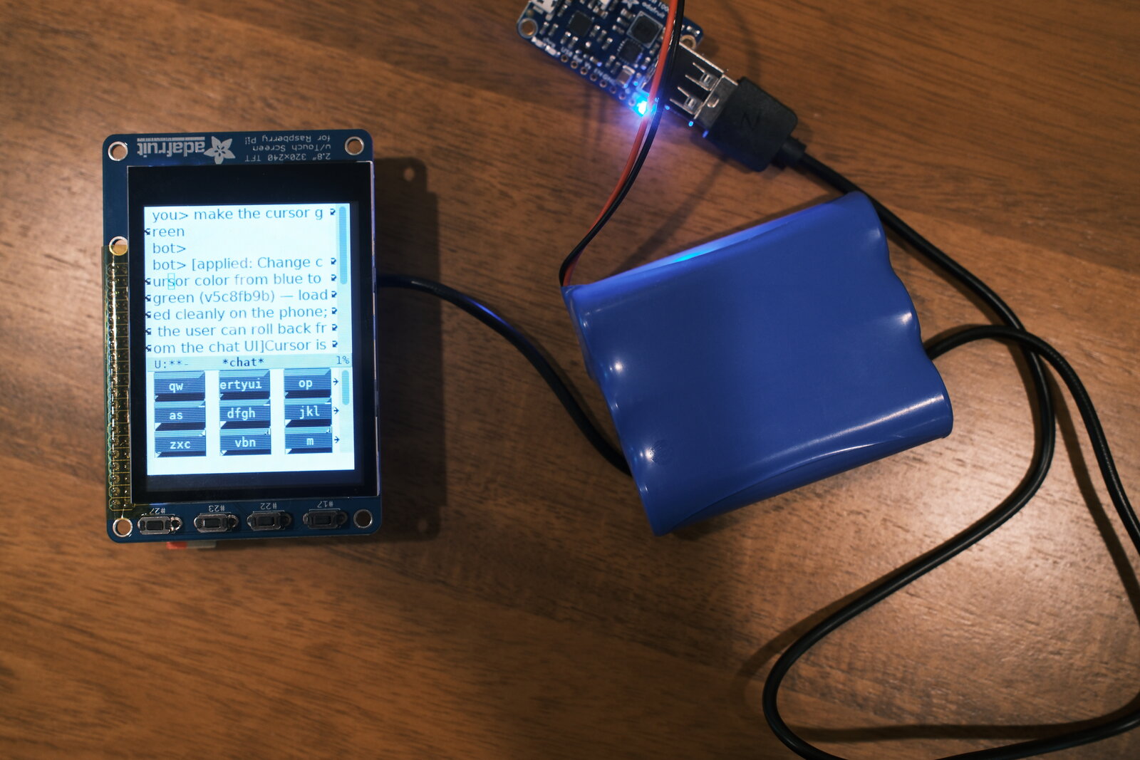 EmacsOS on a Raspberry Pi: a small touchscreen showing a cursor-change chat with the T9 keyboard below, next to a USB battery pack.